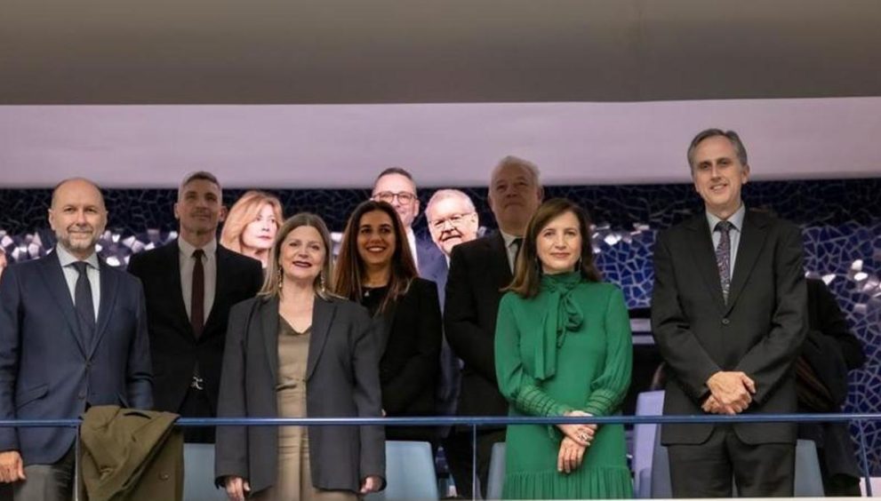 Group of professionals in formal attire posing for a photo at a ceremony, standing behind a blue railing.