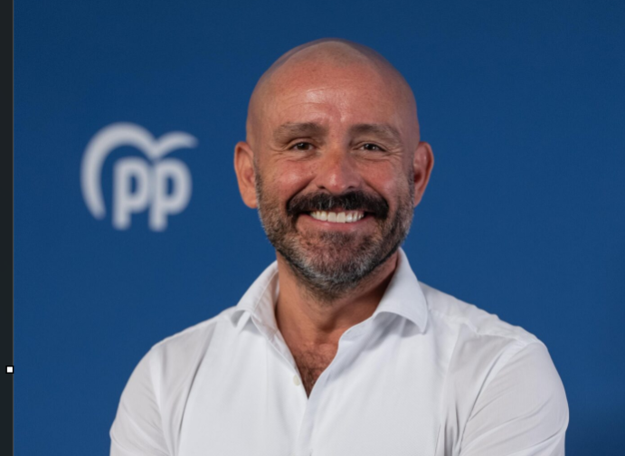 Smiling man in a white shirt poses in front of a blue backdrop with a PP logo on the left.